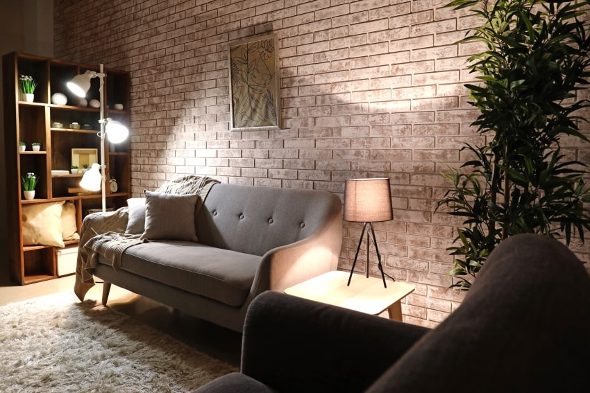 Living room at night with brick wall, wood furniture, lamps, and grey sofa
