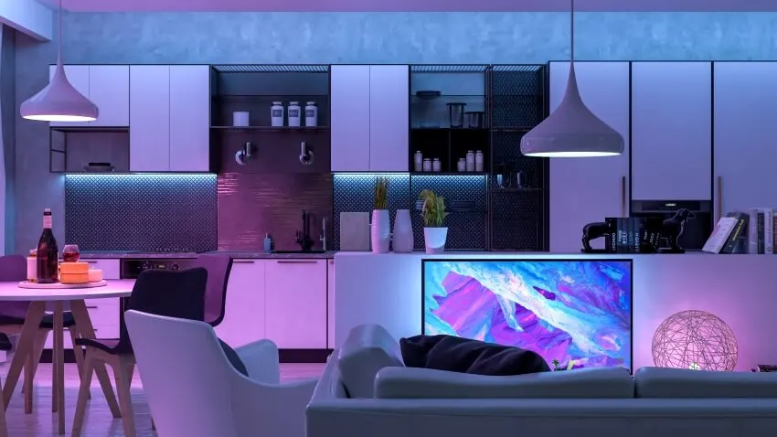 Living room of an open floor apartment with pendant lamps, colored LED light, and white furniture