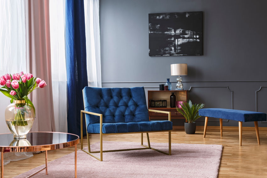 Blue chair, rug, wood floor, dresser, lamp, and window curtain