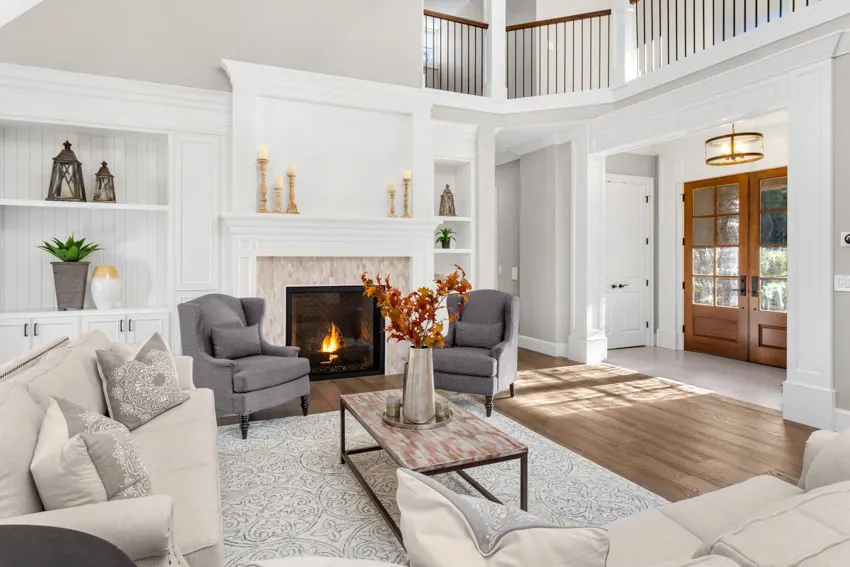 Gray accent chairs, couch, rug, wood floor, fireplace, and front door