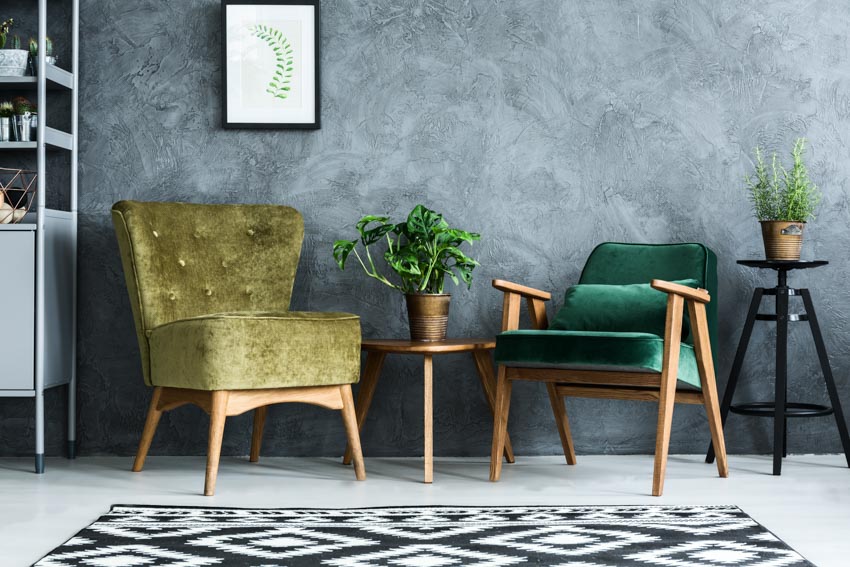 Living room with green accent chairs, floor rug, small tables, indoor plants, and concrete walls