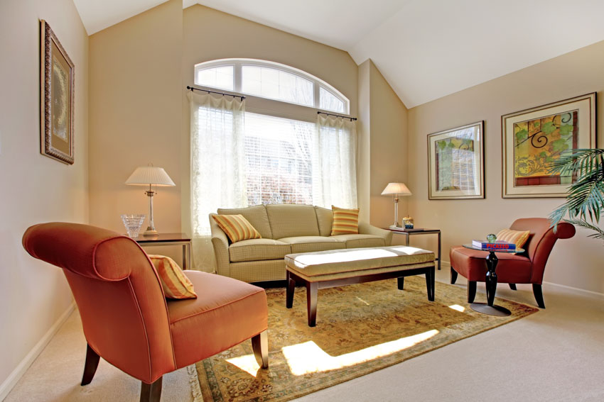 Living room with orange accent chairs, couch lamps, floor rug, and window curtains
