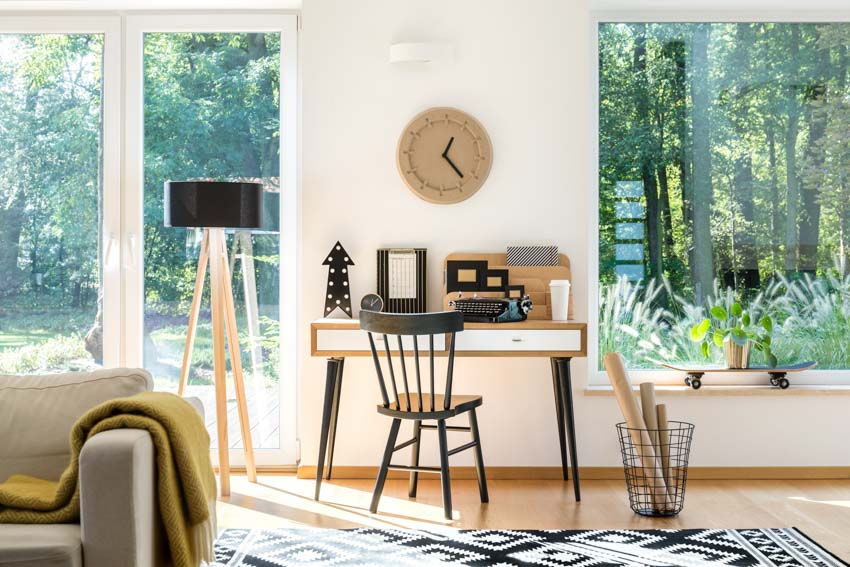 Living room with study area, chair, desk, floor lamp, windows, and wall clock