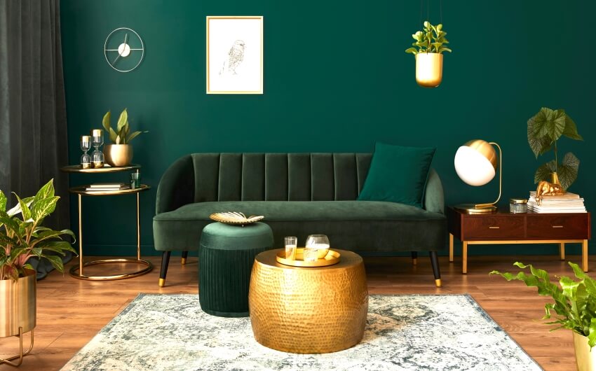 Luxury living room with end tables, green velvet sofa, golden coffee table, pouf, and plants