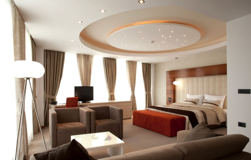 Modern apartment bedroom with sitting area, panoramic windows, and round ceiling with lighting fixtures