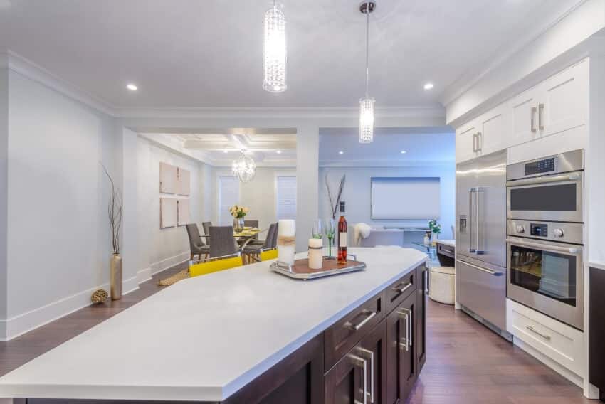 Modern bright kitchen with stainless steel appliances, pendant lights, and white acrylic countertops