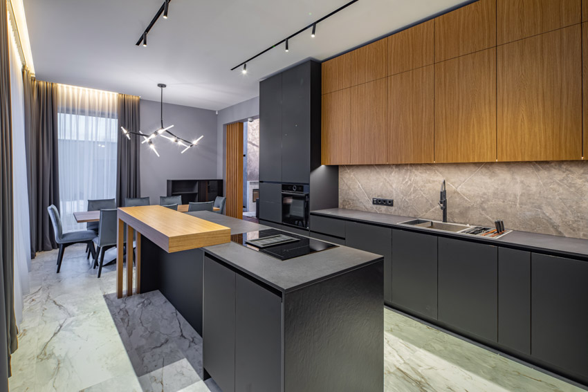 Modern kitchen with black center island, granite backsplash, dining area, and hanging lights
