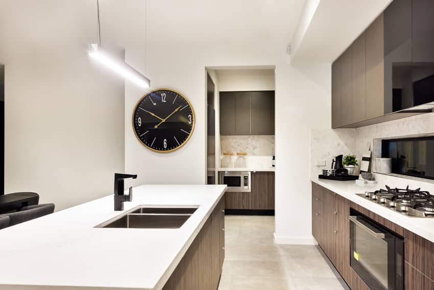 Modern kitchen with black wall clock, center island, countertop, wood cabinets, and hanging lights