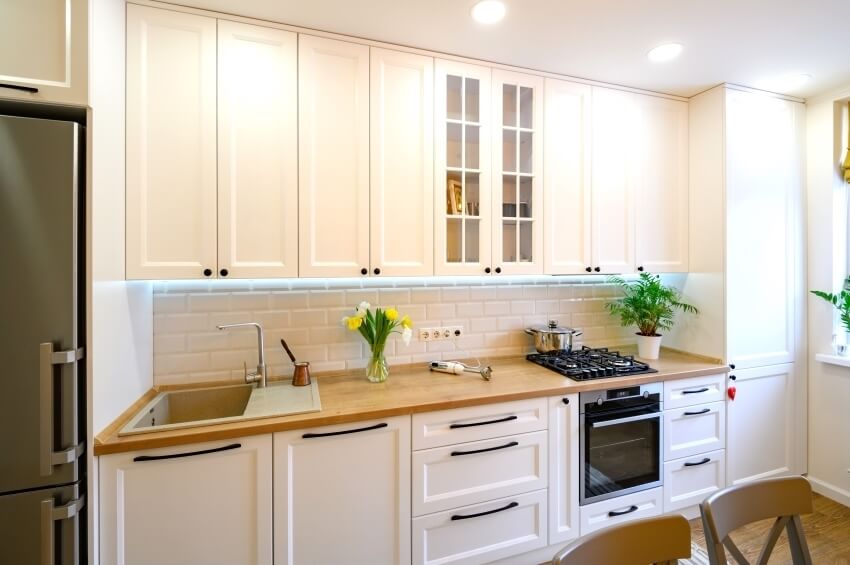 Modern kitchen with wood countertop, subway tile backsplash, and white cabinets with oversized pulls