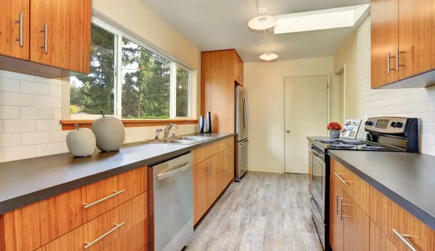 Narrow kitchen with grey acrylic countertops, laminate cabinets, subway tile backsplash, and long windows