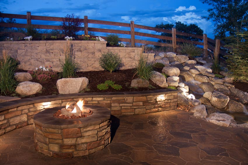 Outdoor area with hardscape lighting, firepit, and hedge plants