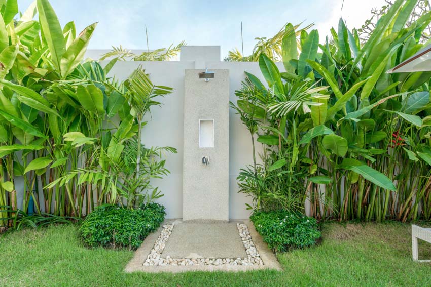 Outdoor area with showerhead, shower floor, white walls, and plants surrounding it