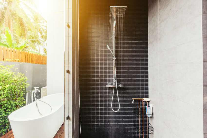 Outdoor bathroom with tub, showerhead, and black tile wall