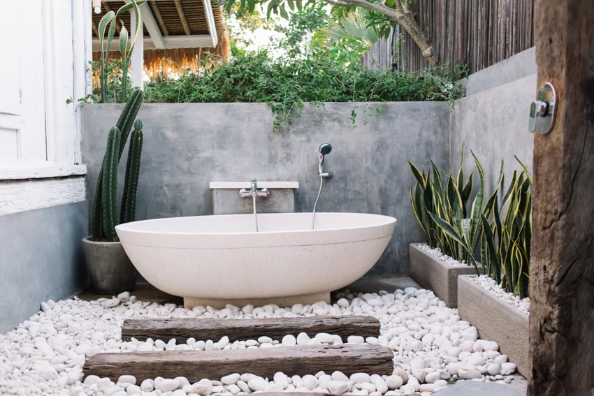 Outdoor bathroom with tub, showerhead, and white stone floor