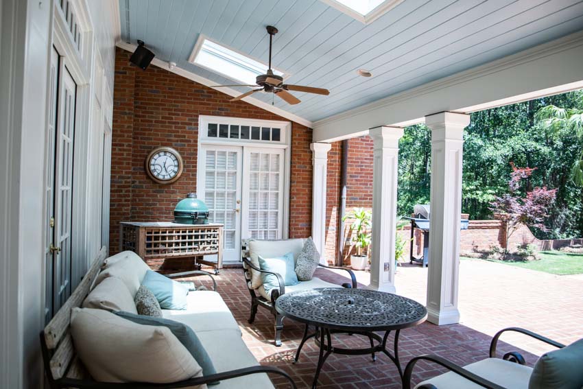 Outdoor patio with brick wall, skylight, clock, ceiling fan, couch, table, and garden