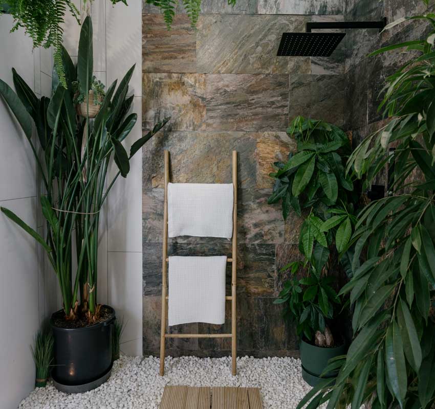 Outdoor shower with stone tile accent wall, black showerhead, pebbled floor, and various types of plants