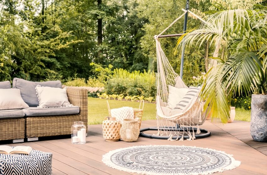 Pillows on hammock chair on terrace with round rug and rattan sofa in the garden