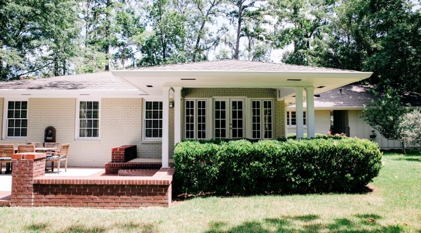 Rear view of house with brick and concrete patio, and landscaped bushes