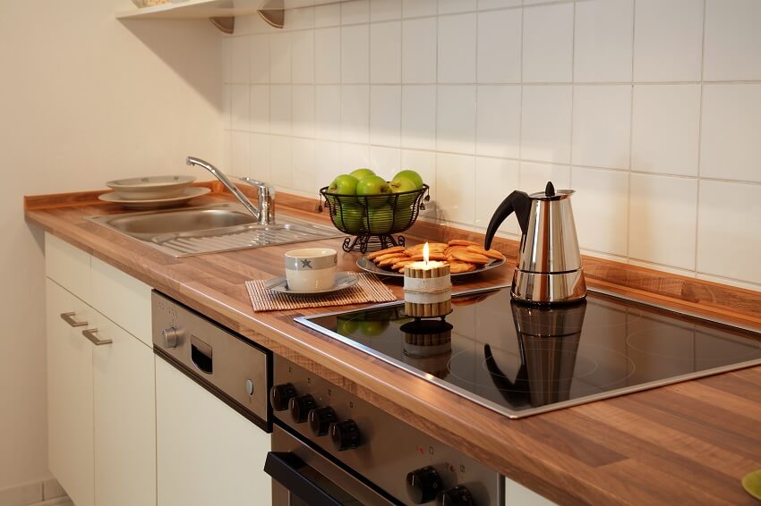Redwood kitchen countertop with sink, a basket of green apples and a kettle on built in stove