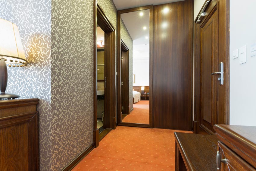 Room with hallway, wallpaper, mirrors, and orange floor