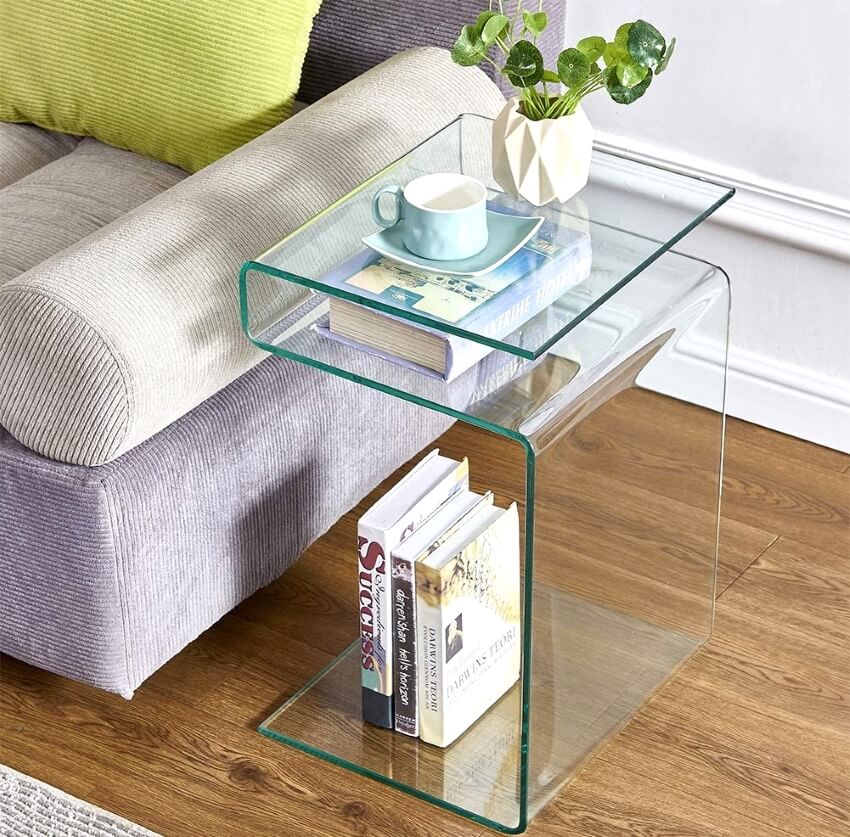 S-shaped glass table with books and flower in a vase beside sofa
