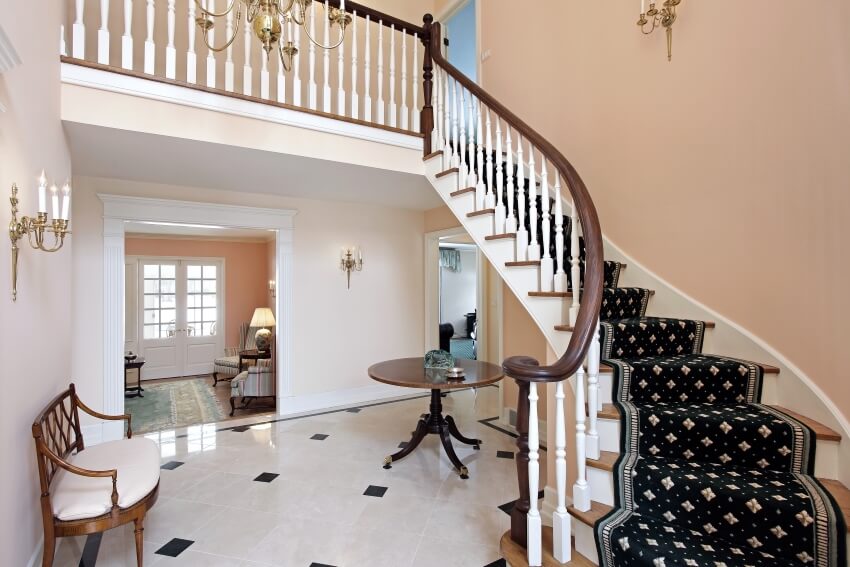 Salmon colored foyer with tile floor, round table, and curved staircase with nylon carpet runner