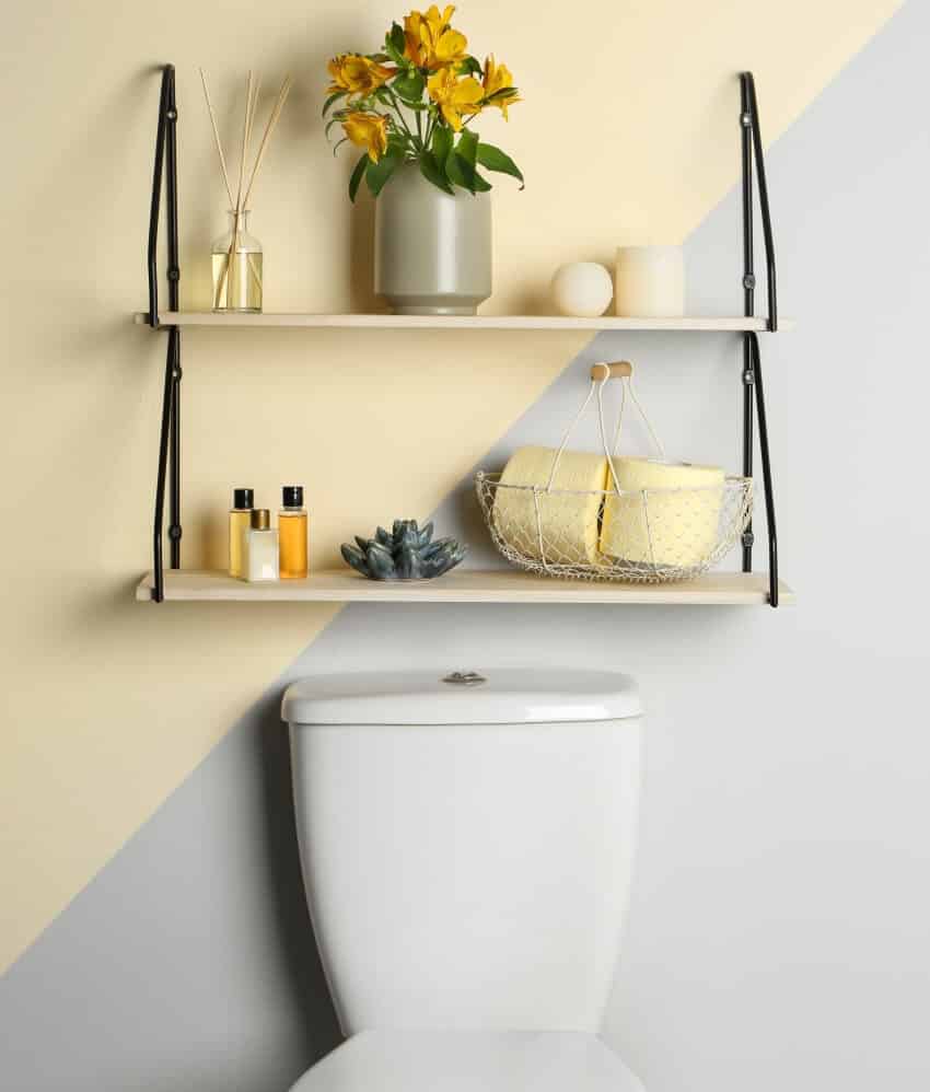 Shelves with different decorations on wall above toilet tank in restroom interior