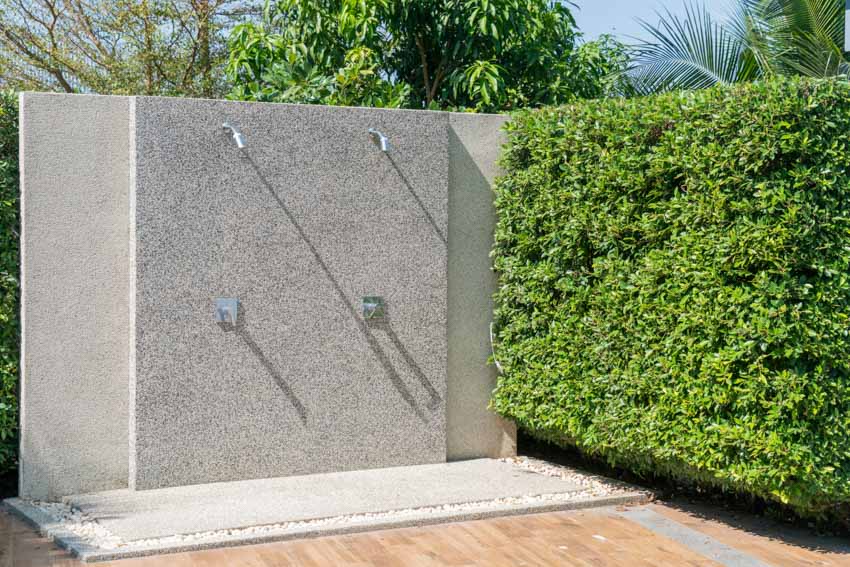 Simple outdoor shower with concrete wall, and hedge plants
