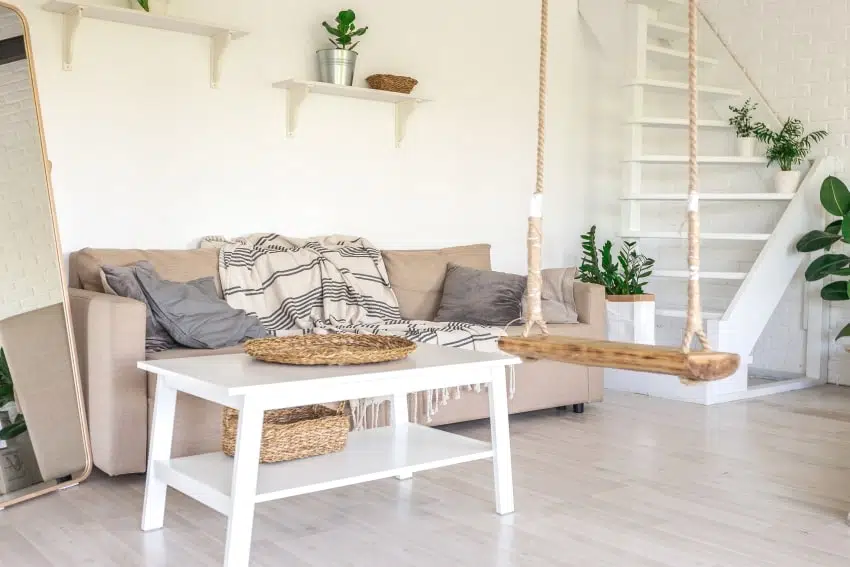 Sitting area in a white room with a traditional coffee table, rope swing, and floating shelves
