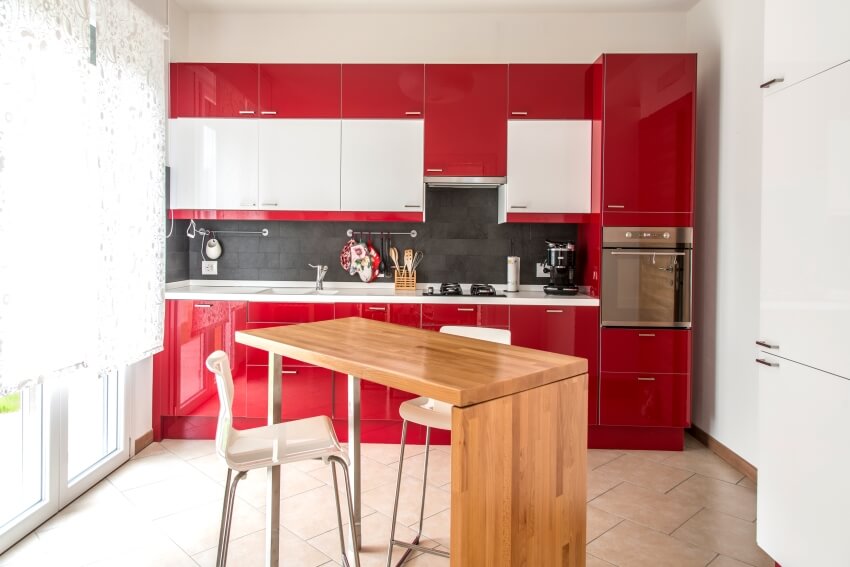 Small kitchen with red glossy cabinets, tile floors, and wooden island with chairs