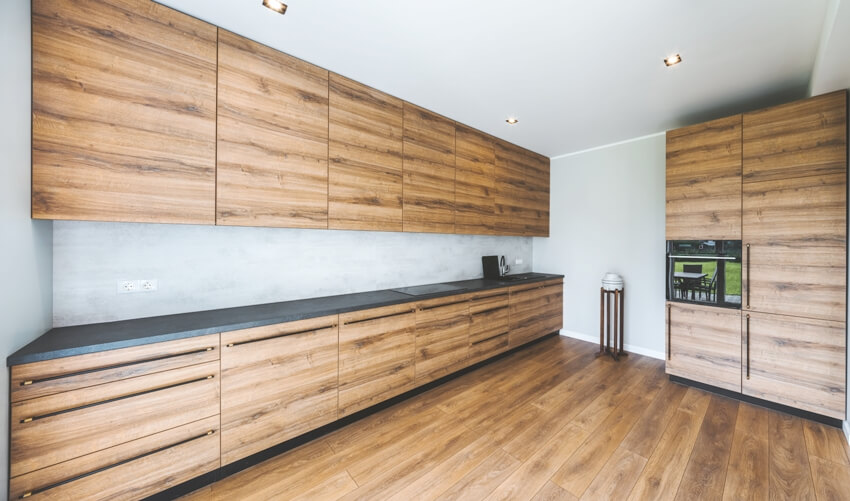 Spacious empty kitchen with hardwood floors, dark grey countertop, and laminate cabinets