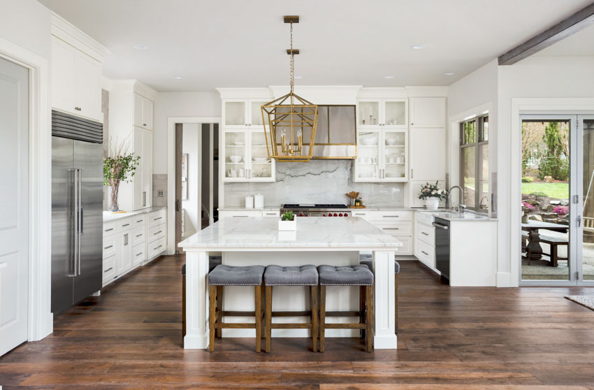 Spacious kitchen with dark wood flooring, white cabinetry, center island, chairs, and backsplash