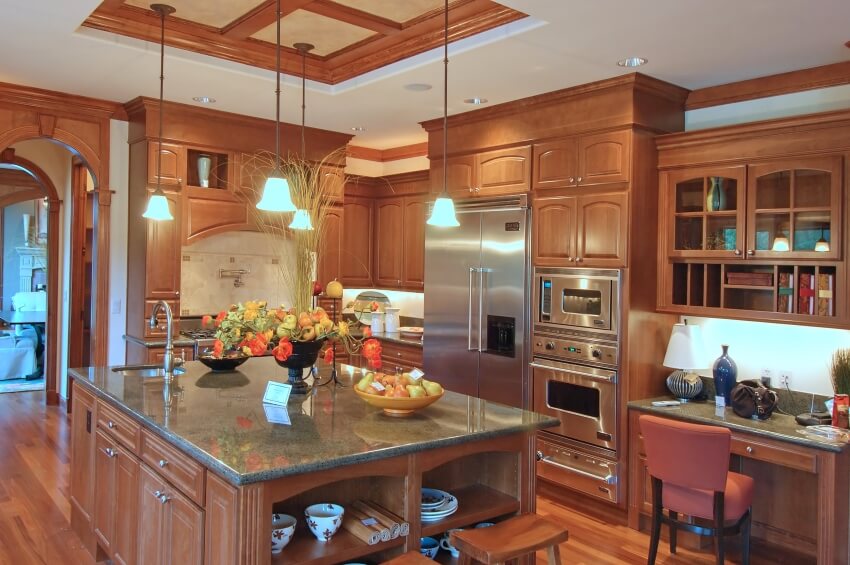Spacious kitchen with pendant lights above large island, coffered ceiling, and cherry cabinets