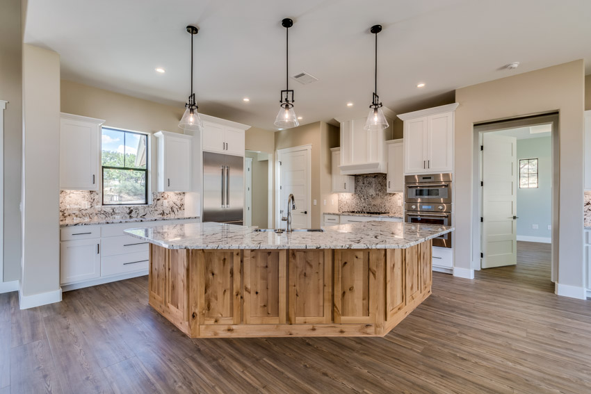 Spacious kitchen with center island, wood floor, pendant lights, backsplash, and white cabinets