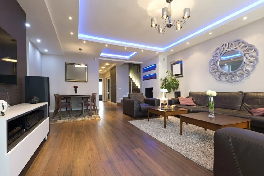 Spacious living room with wood floor, leather sofa, coffee tables, and blue modern ceiling light