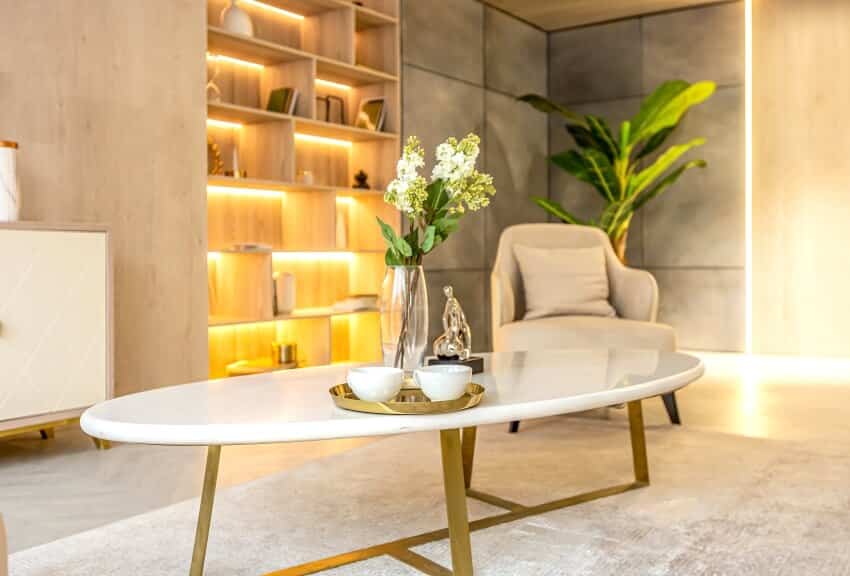 Studio apartment living room with built-in lighting in shelves, armchair, and coffee table with golden base