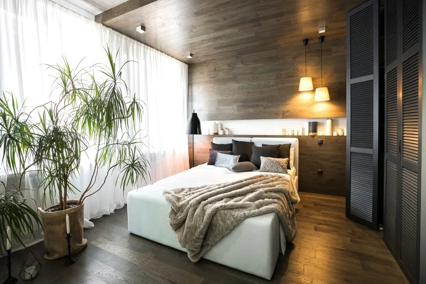 Stylish bedroom with a black wardrobe, large window, sheer curtains, wooden walls pendant lamps and plants