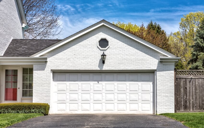 Traditional two car wooden garage with wall mounted lamp, and white brick exterior
