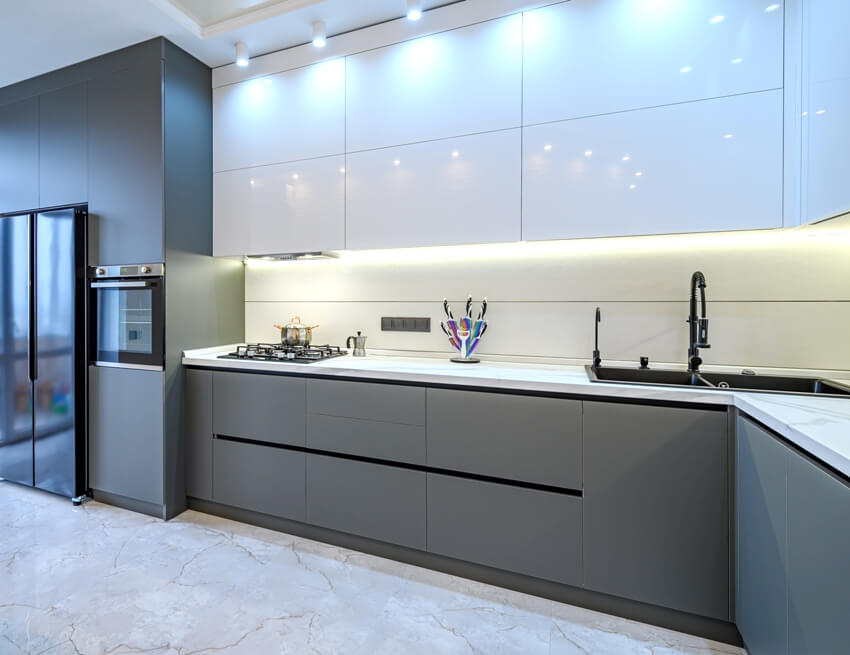White and dark grey modern kitchen interior with under cabinet lighting, marble floor, and dining table