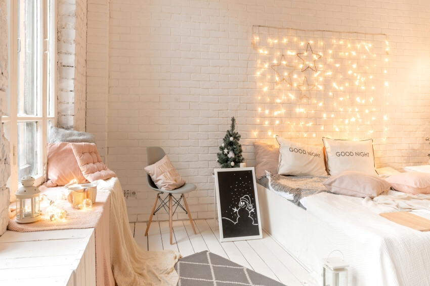 White bedroom with fairy lights on brick wall, panel floor, and a built-in bench by the window