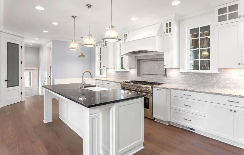 White kitchen with large island, marble and granite countertops, pendant lights, and hardwood floors