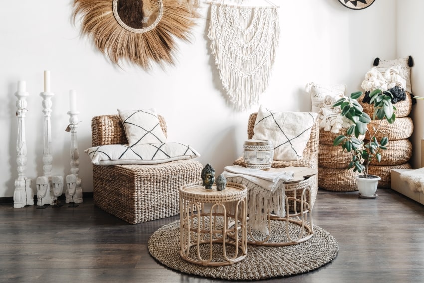 Wicker furniture, rattan coffee table and armchair with cushions, and macrame on white wall of living room