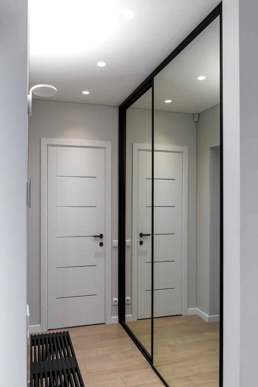 A hallway with black bench, wardrobe with large mirror and recessed lighting