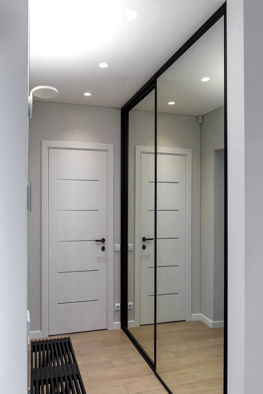A hallway with black bench and wardrobe with large mirror 