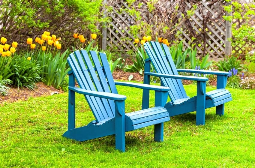 A pair of blue wooden adirondack chairs in the spring garden