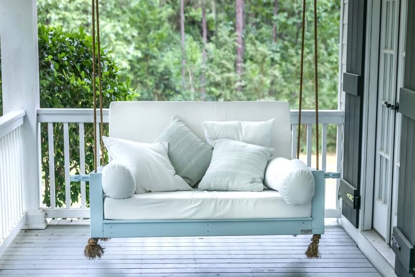 A porch with wooden floor and white swinging bench with pillows