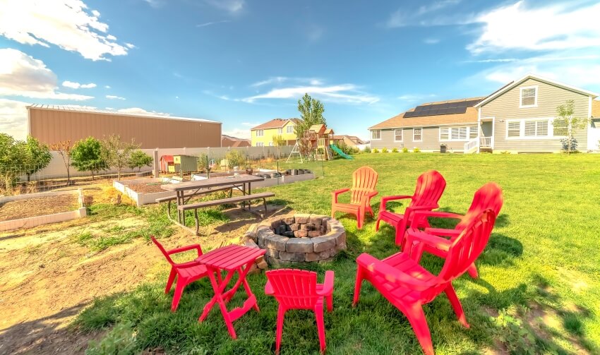 Adirondack chairs around a stone fire pit adjacent to a picnic table with bench at the backyard