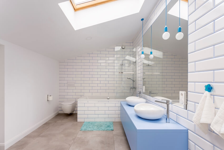Attic bathroom with subway tile walls, skylight window, and washbasins on blue painted countertops