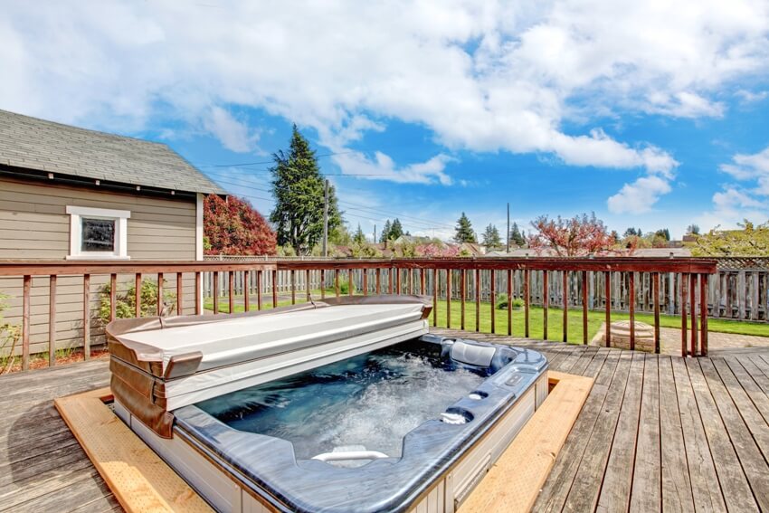 Backyard wooden deck with hot tub on it and a nice blue sky view