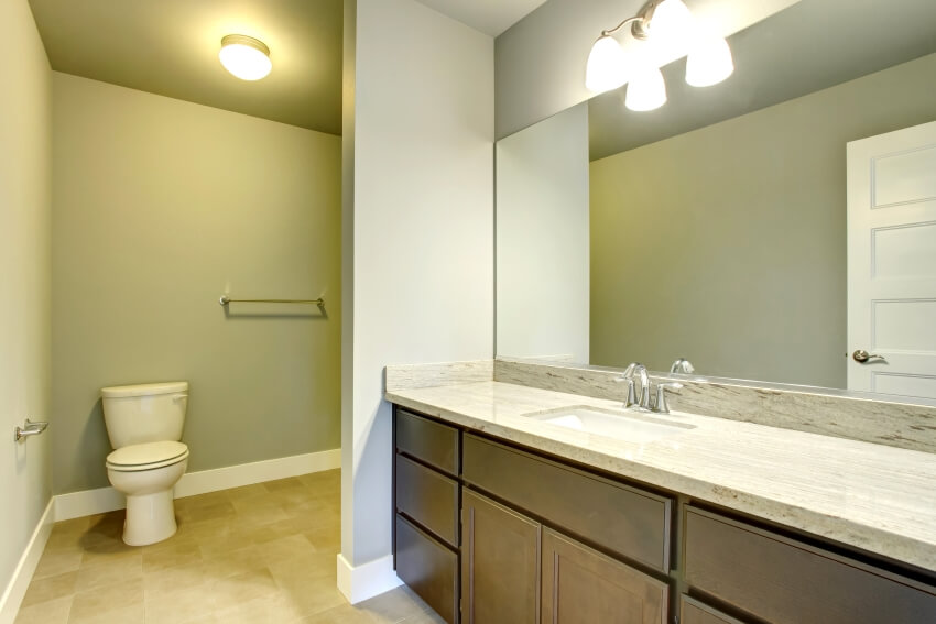 Bathroom with wall sconce, large mirror, and toilet partition